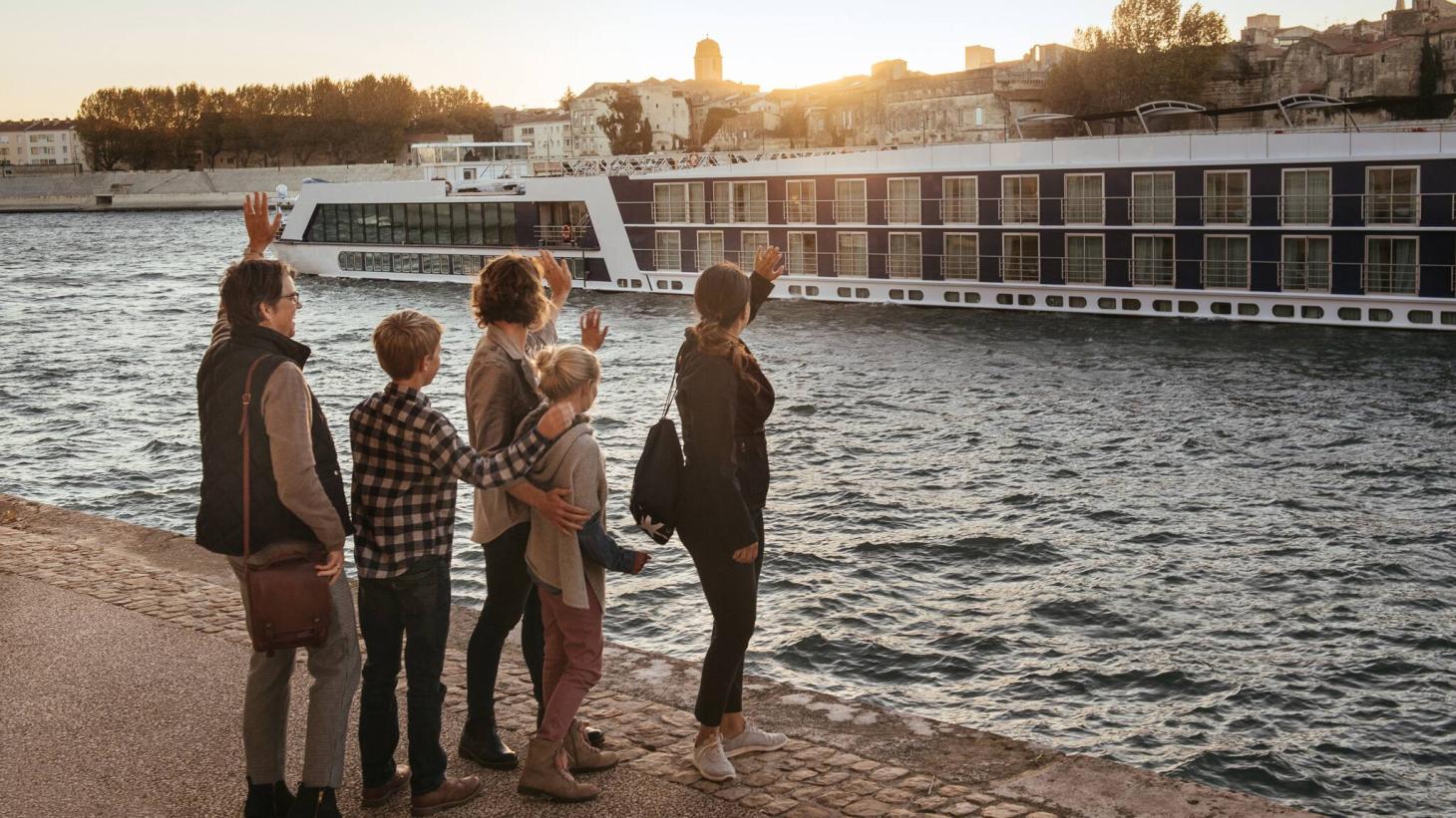 Family waving at Adventures by Disney river cruise ship at sunset